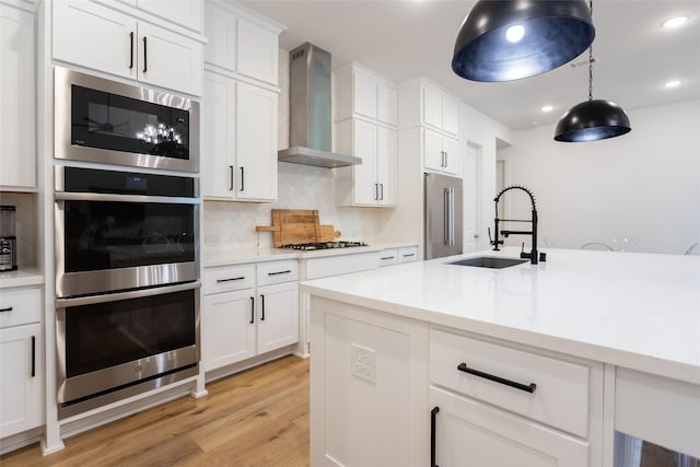 kitchen with appliances with stainless steel finishes, sink, wall chimney range hood, and white cabinets