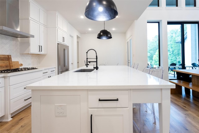 kitchen with an island with sink, sink, high end refrigerator, and wall chimney range hood