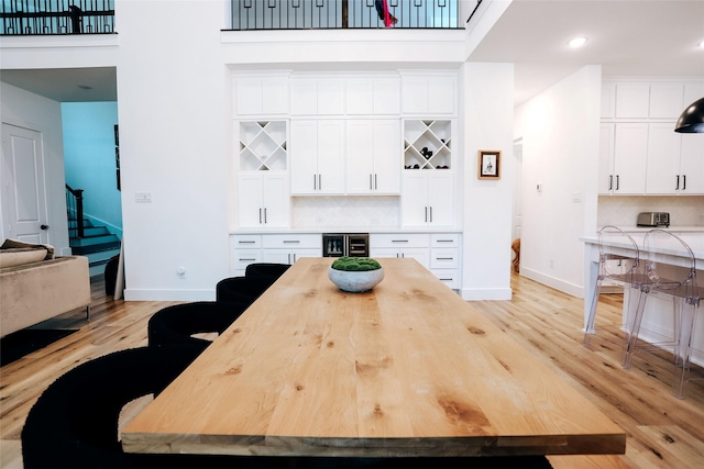 dining space with a high ceiling, indoor bar, beverage cooler, and light wood-type flooring