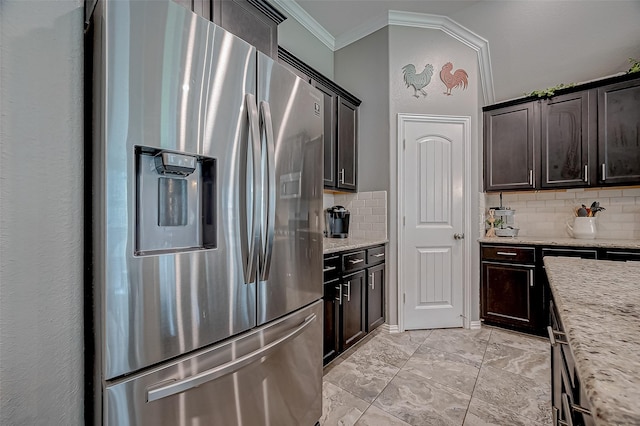 kitchen with tasteful backsplash, ornamental molding, stainless steel fridge, and light stone counters