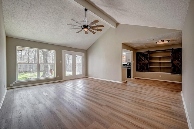 unfurnished living room with a barn door, vaulted ceiling with beams, a textured ceiling, and light hardwood / wood-style flooring