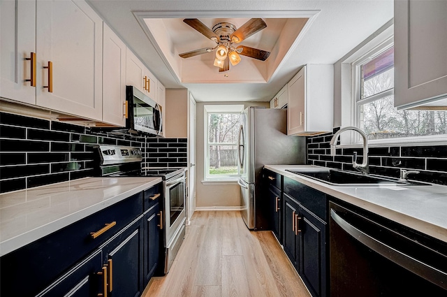 kitchen featuring a raised ceiling, blue cabinets, white cabinets, stainless steel appliances, and light wood-type flooring