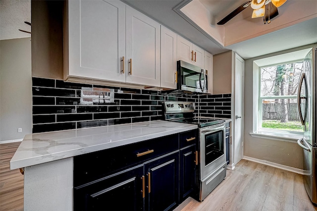 kitchen featuring white cabinetry, light hardwood / wood-style flooring, appliances with stainless steel finishes, light stone countertops, and decorative backsplash