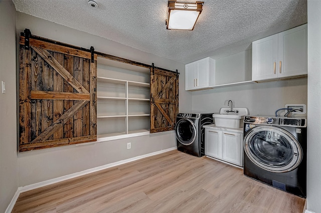 laundry room featuring sink, light hardwood / wood-style flooring, cabinets, separate washer and dryer, and a barn door