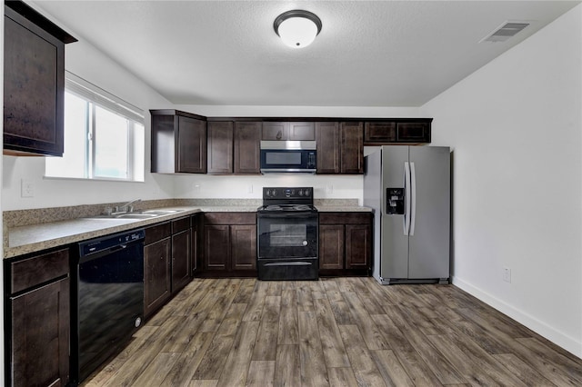 kitchen with sink, a textured ceiling, dark brown cabinets, hardwood / wood-style flooring, and black appliances