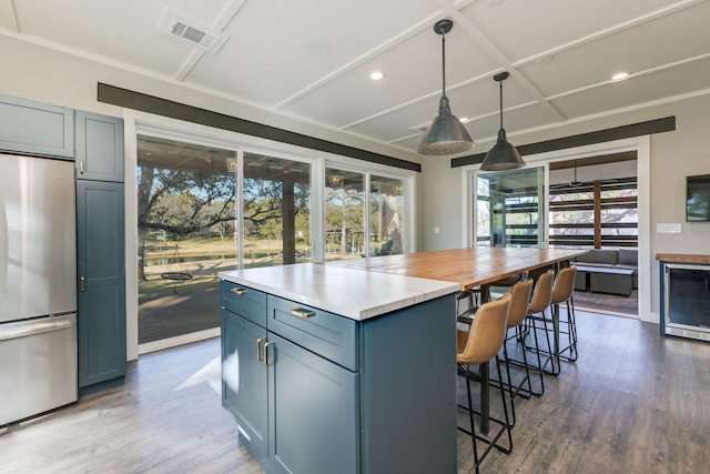 kitchen with wine cooler, stainless steel refrigerator, a kitchen breakfast bar, pendant lighting, and hardwood / wood-style floors