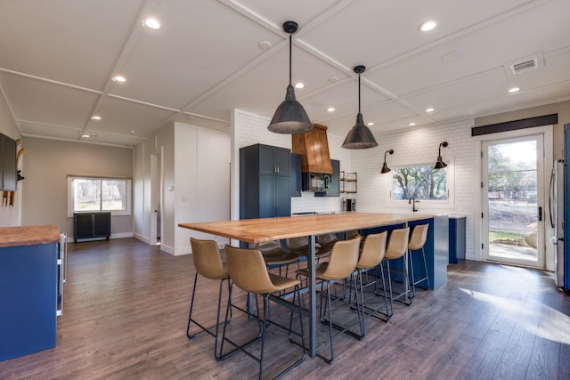 kitchen with dark wood-type flooring, butcher block counters, stainless steel fridge, a kitchen breakfast bar, and pendant lighting