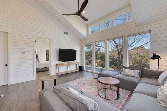 living room with plenty of natural light, hardwood / wood-style floors, high vaulted ceiling, and wood walls