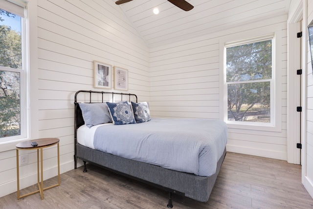 bedroom featuring lofted ceiling, wooden walls, light hardwood / wood-style floors, and multiple windows