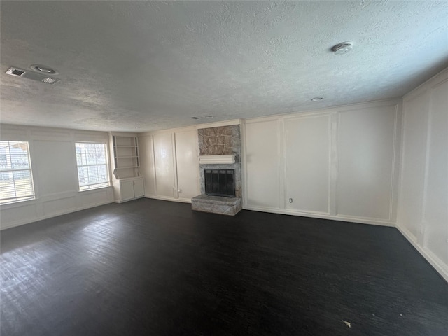 unfurnished living room with a stone fireplace, dark wood-type flooring, built in features, and a textured ceiling