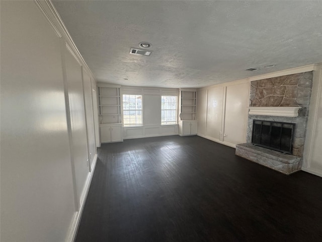 unfurnished living room featuring built in shelves, a fireplace, dark wood-type flooring, and a textured ceiling