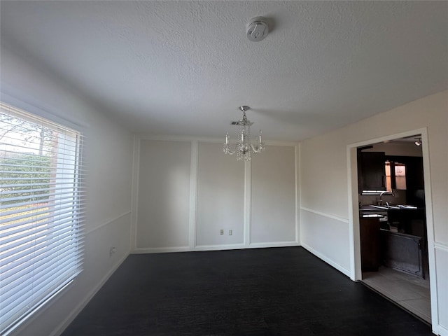 empty room featuring an inviting chandelier, dark wood-type flooring, and a textured ceiling