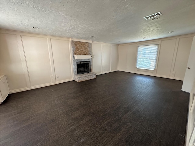 unfurnished living room with dark wood-type flooring, a stone fireplace, and a textured ceiling