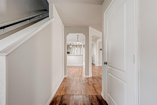 hall with arched walkways, wood finished floors, and baseboards