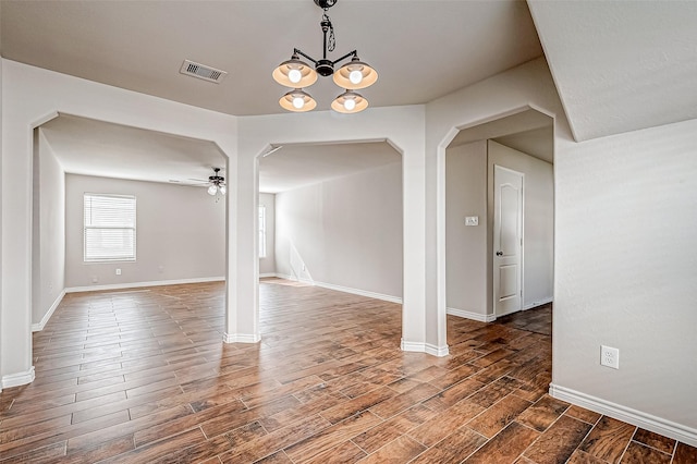 empty room with dark wood-style floors, ceiling fan with notable chandelier, arched walkways, and visible vents