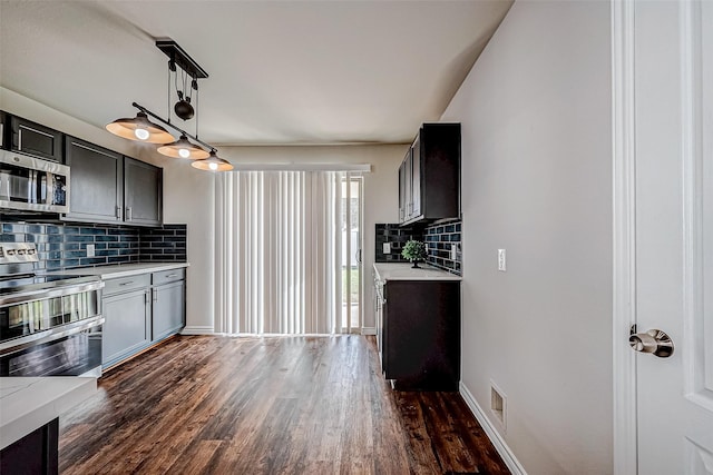 kitchen with stainless steel appliances, pendant lighting, light countertops, and dark wood finished floors