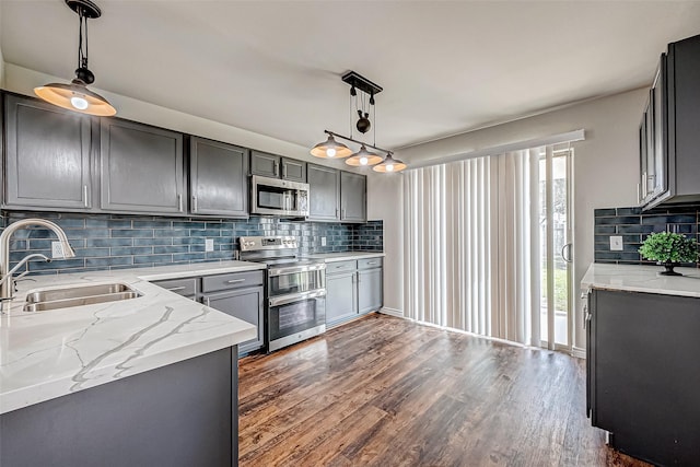 kitchen with light stone counters, stainless steel appliances, a sink, gray cabinets, and decorative light fixtures