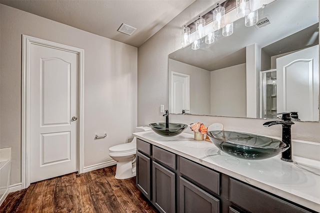 full bath with double vanity, visible vents, a sink, and wood finished floors