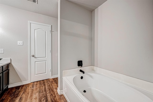 bathroom featuring vanity, wood finished floors, a bath, and baseboards