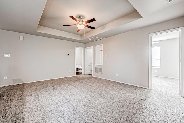 carpeted empty room with baseboards, visible vents, a raised ceiling, and a ceiling fan