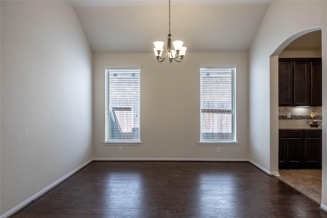 unfurnished dining area with a notable chandelier, vaulted ceiling, and dark hardwood / wood-style floors