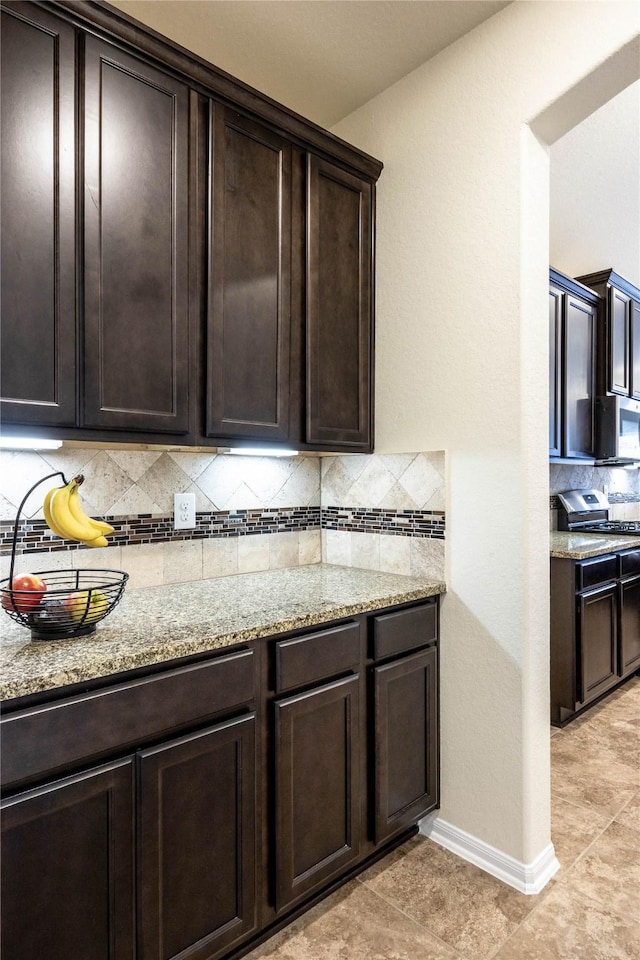 kitchen with dark brown cabinetry, light stone counters, tasteful backsplash, and stainless steel appliances