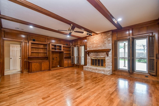 unfurnished living room with ceiling fan, a fireplace, beam ceiling, and light wood-type flooring