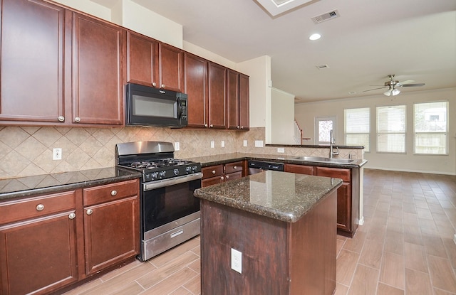 kitchen featuring sink, dark stone countertops, appliances with stainless steel finishes, a kitchen island, and decorative backsplash