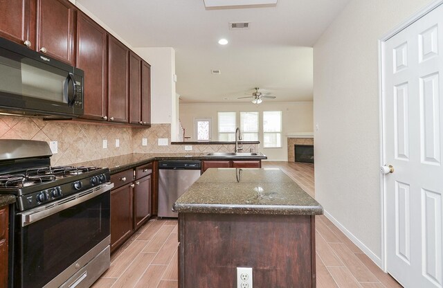 kitchen with sink, a center island, dark stone counters, stainless steel appliances, and backsplash