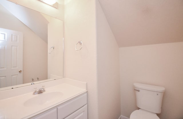 bathroom with lofted ceiling, vanity, and toilet