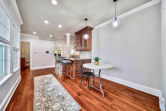 kitchen featuring a breakfast bar, crown molding, stone countertops, pendant lighting, and decorative backsplash