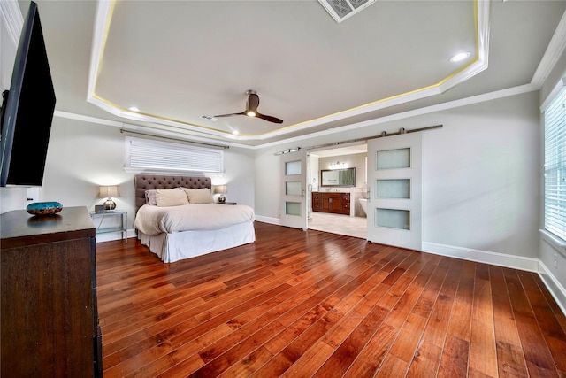 bedroom featuring hardwood / wood-style floors, connected bathroom, ornamental molding, a raised ceiling, and a barn door