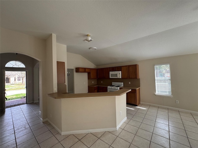 kitchen featuring white appliances, lofted ceiling, kitchen peninsula, and light tile patterned floors