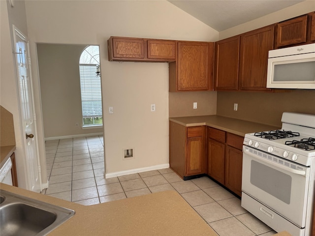 kitchen featuring white appliances, sink, vaulted ceiling, and light tile patterned floors