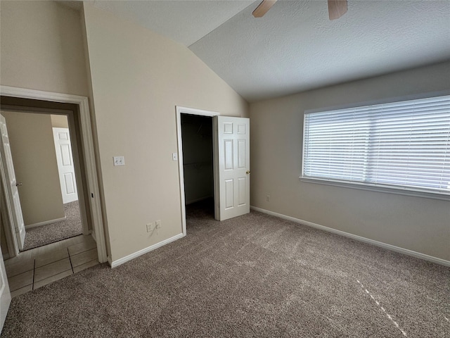 unfurnished bedroom featuring vaulted ceiling, carpet flooring, a spacious closet, ceiling fan, and a textured ceiling