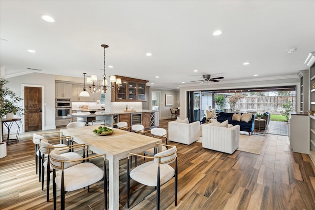 dining room featuring sink, crown molding, hardwood / wood-style floors, wine cooler, and ceiling fan with notable chandelier