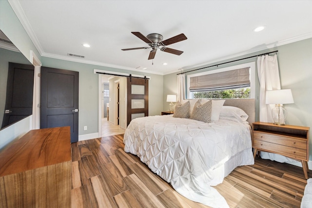 bedroom featuring ornamental molding, a barn door, ceiling fan, and light wood-type flooring