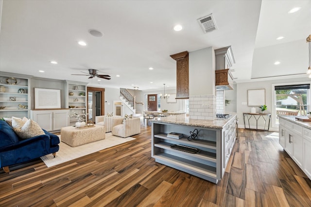 kitchen featuring dark wood-type flooring, hanging light fixtures, light stone countertops, white cabinets, and decorative backsplash