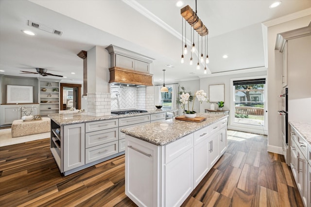 kitchen with appliances with stainless steel finishes, white cabinets, hanging light fixtures, ornamental molding, and a center island