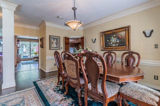 dining room featuring dark wood-type flooring, crown molding, a textured ceiling, and ornate columns