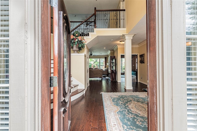 entrance foyer featuring dark wood-type flooring, a towering ceiling, ornamental molding, and ornate columns