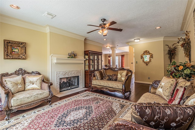 living room featuring ceiling fan, decorative columns, dark hardwood / wood-style floors, ornamental molding, and a textured ceiling