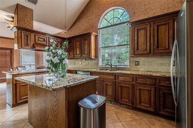 kitchen with sink, light tile patterned floors, stainless steel appliances, a center island, and light stone countertops