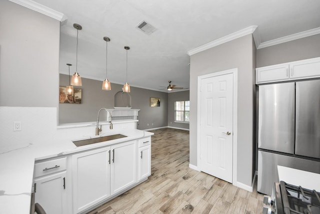 kitchen with sink, white cabinets, stainless steel fridge, hanging light fixtures, and light wood-type flooring