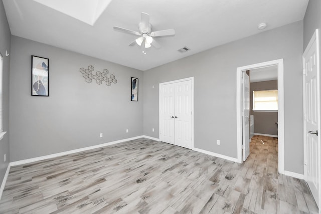 unfurnished bedroom with a skylight, a closet, ceiling fan, and light hardwood / wood-style flooring