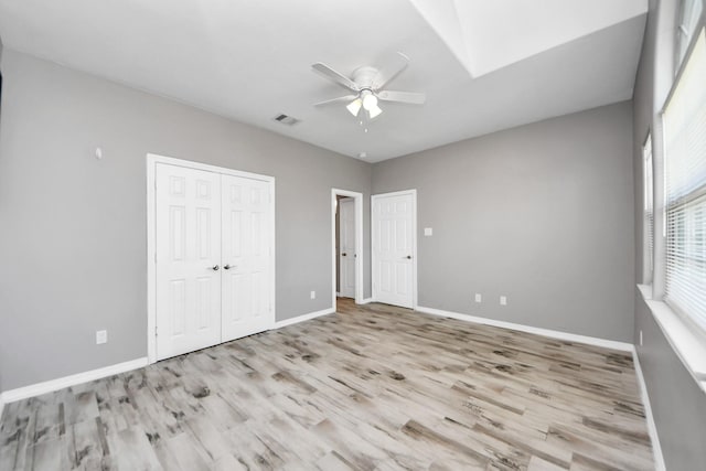 unfurnished bedroom with ceiling fan, a skylight, and light wood-type flooring