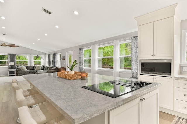 kitchen with a breakfast bar area, vaulted ceiling, light wood-type flooring, black electric cooktop, and white cabinets