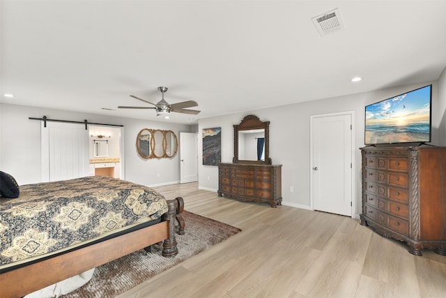 bedroom featuring a barn door, ensuite bath, ceiling fan, and light hardwood / wood-style flooring