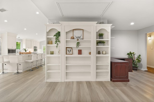 bar with white cabinetry, sink, light hardwood / wood-style floors, and appliances with stainless steel finishes