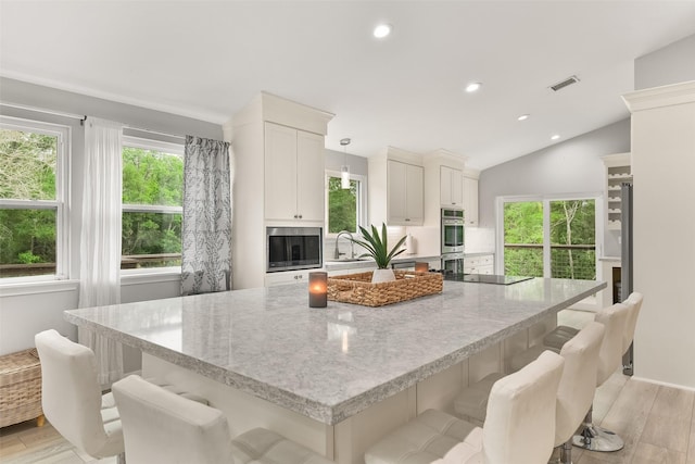 kitchen featuring a spacious island, light stone counters, hanging light fixtures, light wood-type flooring, and black electric cooktop